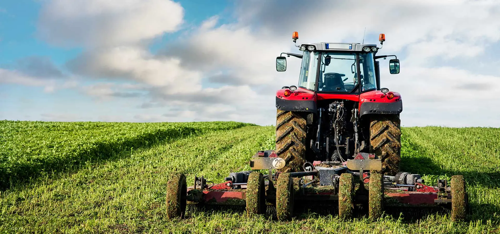 Red tractor pulling a wide batwing mower through a green field