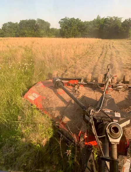 View from behind a tractor cutting a wide swath through dry grass